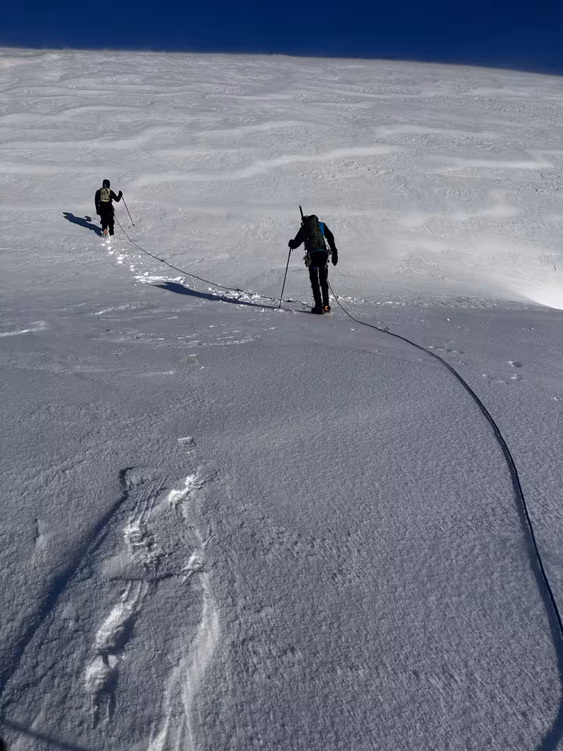 Two climbers roped together ascending snowy Snaefellsjokull glacier under clear blue sky