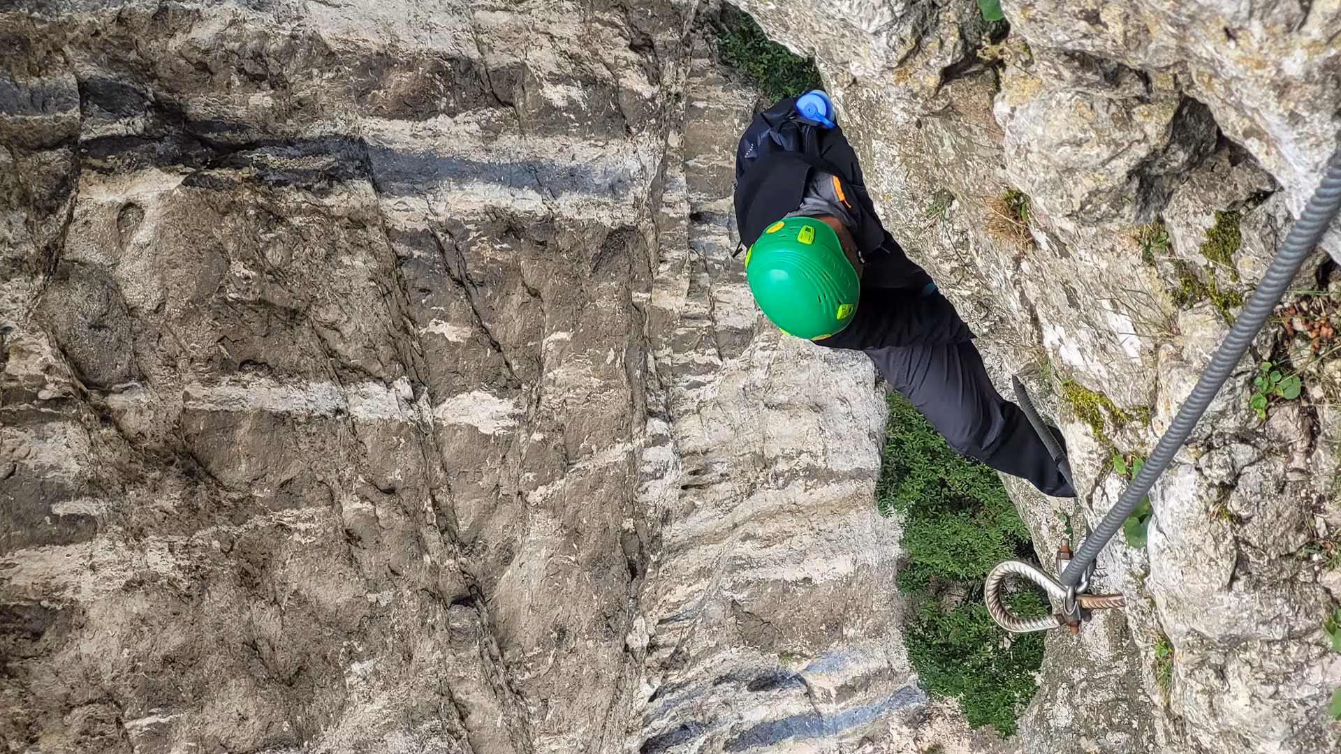 Climber in green helmet ascending steep rocky wall with fixed cable in Turda Canyon