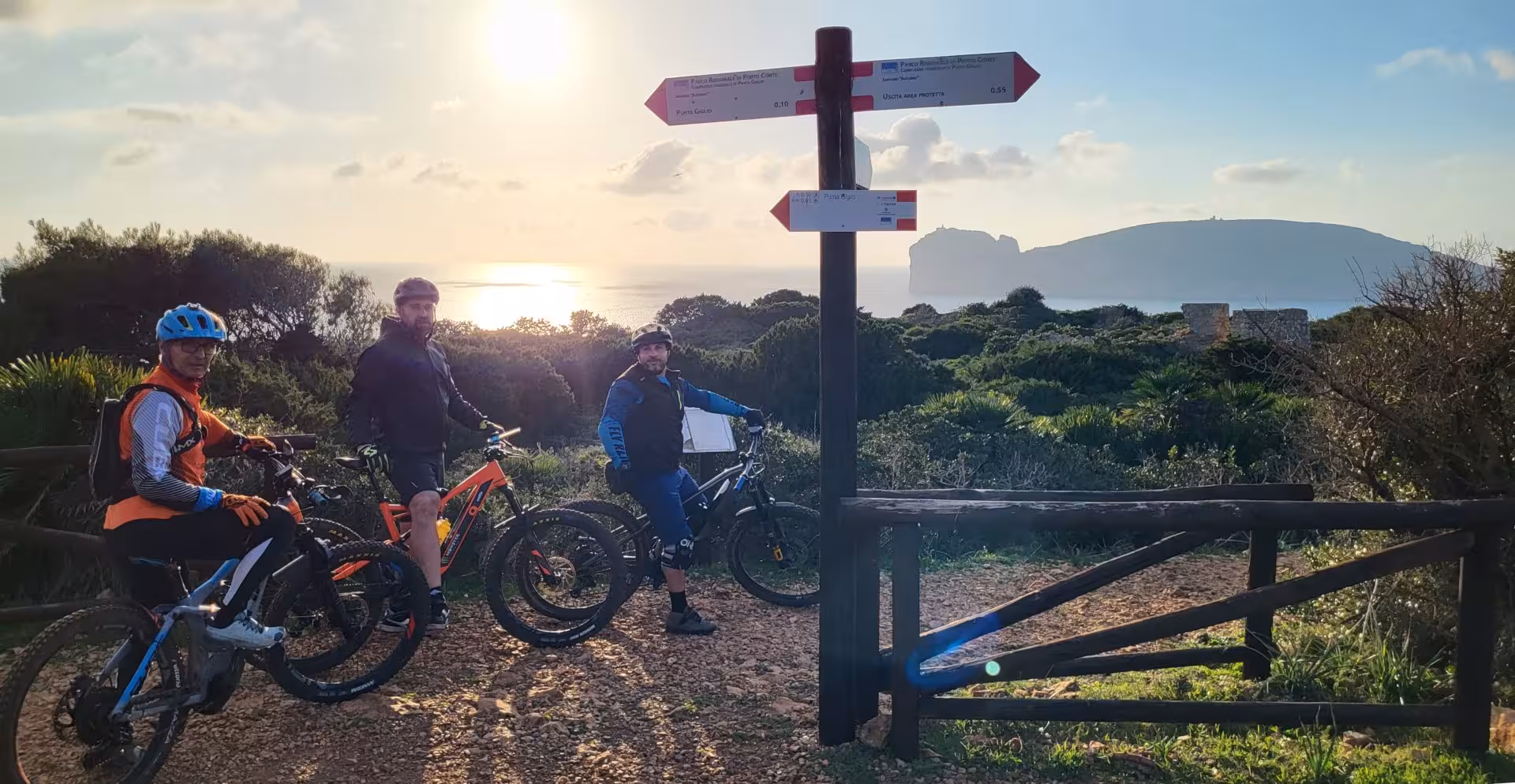 Group of cyclists posing on e-bikes at Alghero coastline viewpoint, ready for an adventurous guided tour.