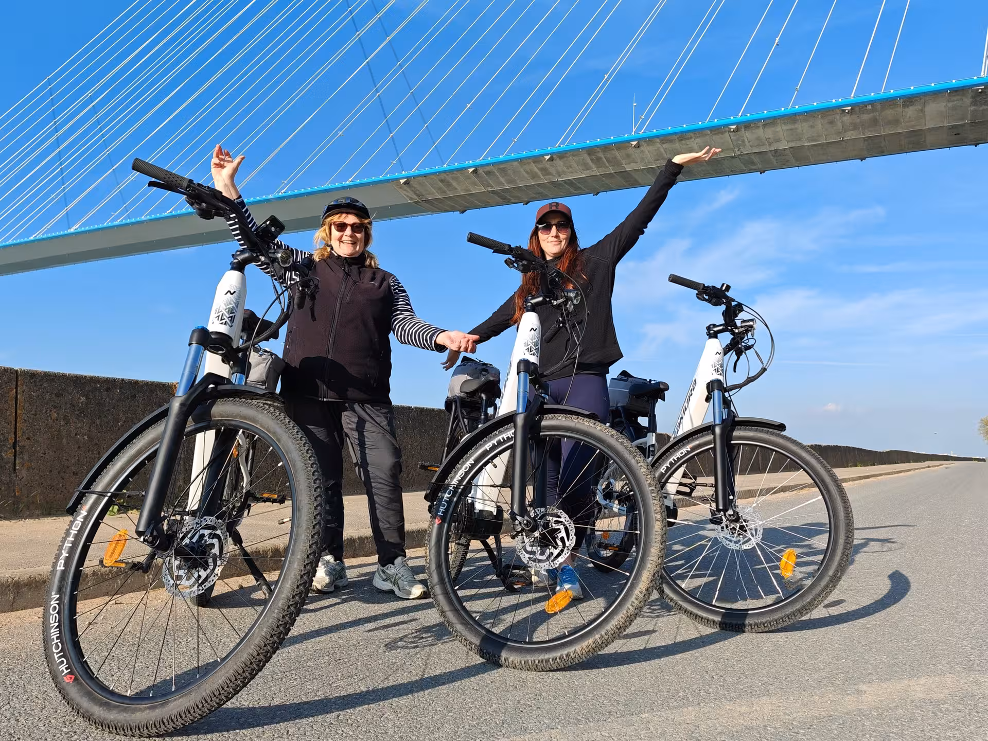 Riders posing with electric bikes under Pont de Normandie, highlight of a guided Honfleur e-bike tour