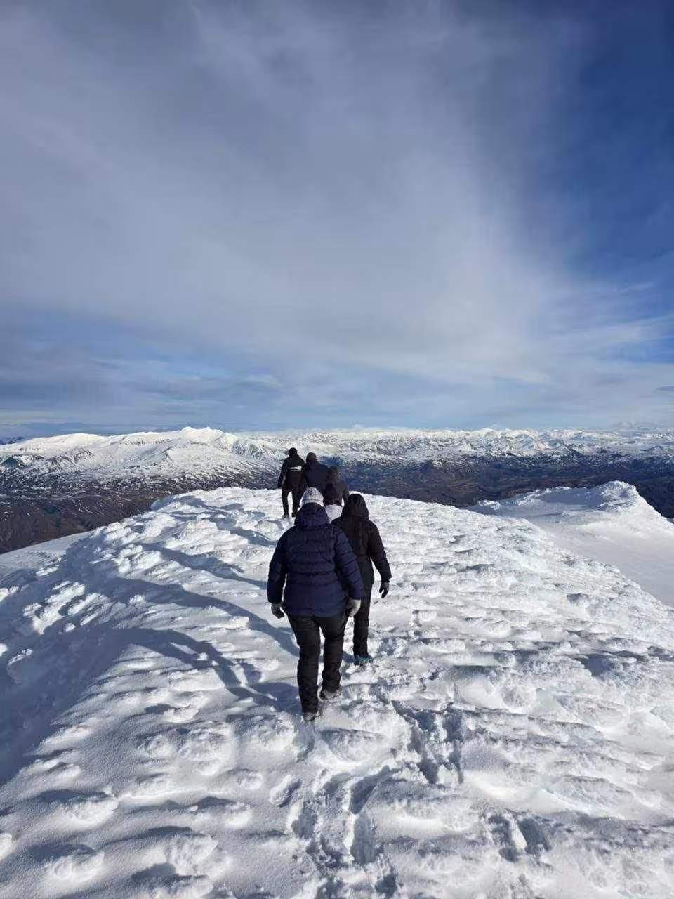 Group of hikers walking across a snowy glacier ridge with mountain panorama in Iceland
