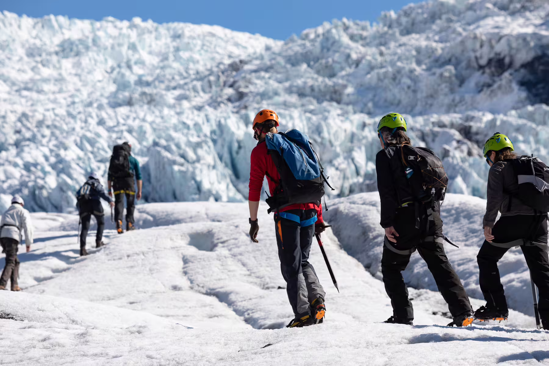 Group of hikers with helmets and ice axes walking on Skaftafell glacier with icefall in background