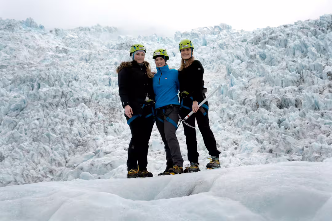 Three women in helmets and harnesses posing on Skaftafell glacier during guided hike