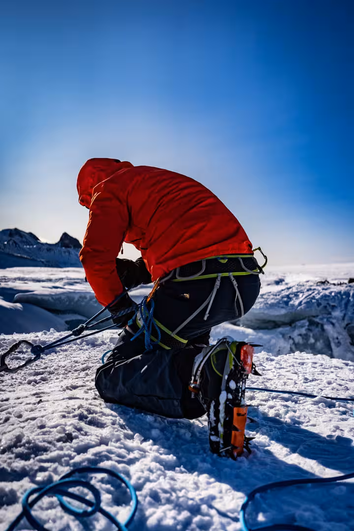Climber in red jacket adjusting crampons on Solheimajokull glacier in Iceland