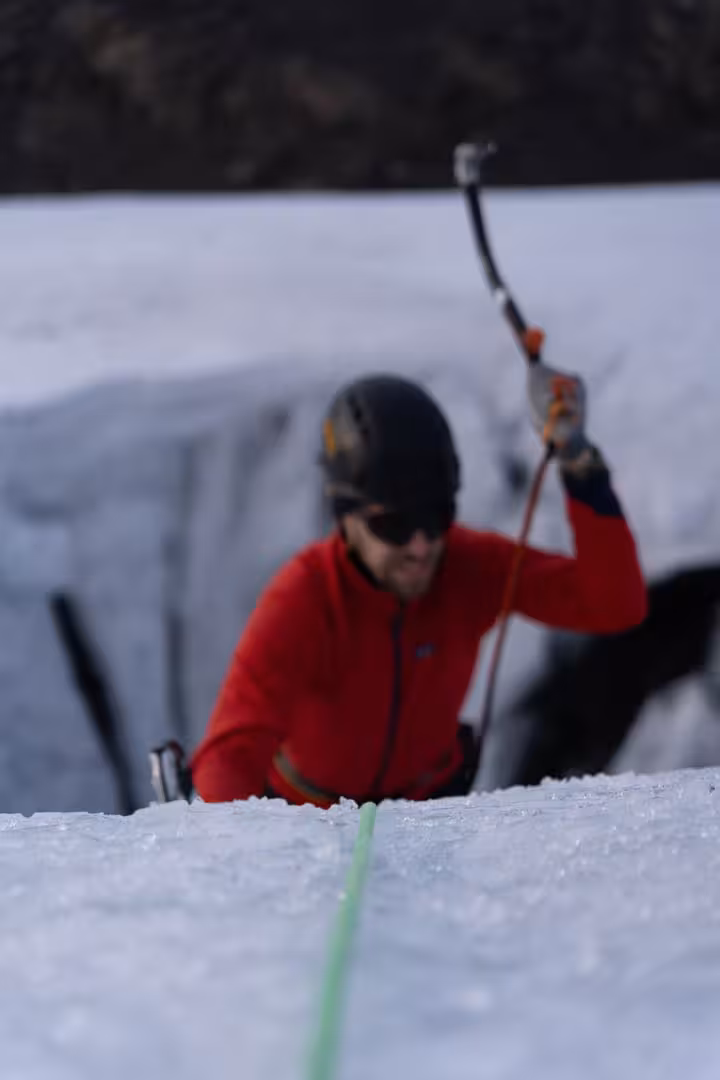 Climber in red jacket ascending glacier with ice axe on Solheimajokull Iceland