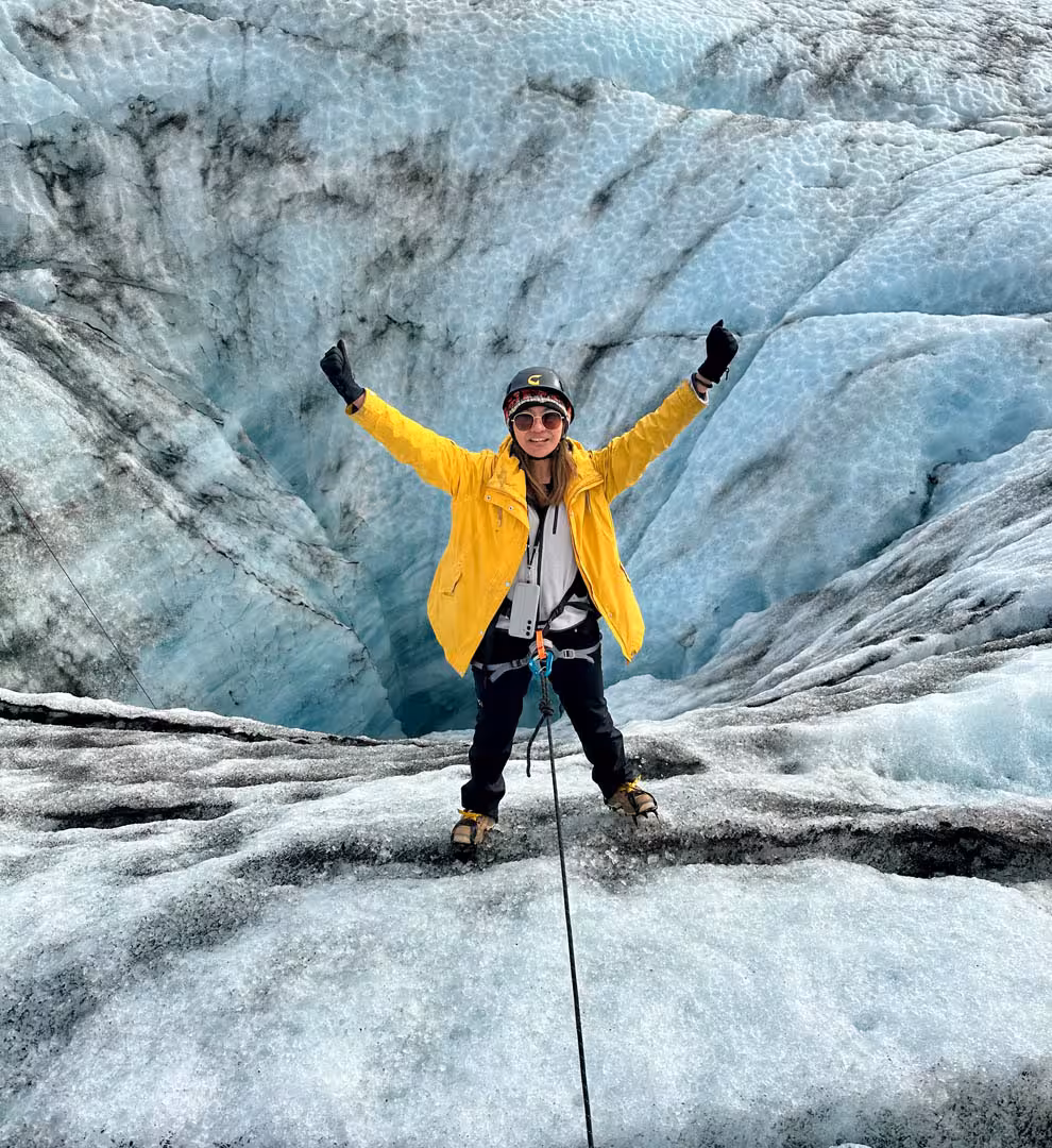 Hiker in yellow jacket with arms raised on Solheimajokull glacier ice wall in Iceland