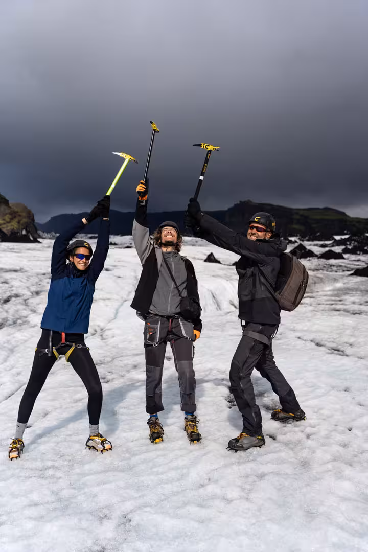 Three hikers celebrating on Solheimajokull glacier with ice axes and crampons in Iceland