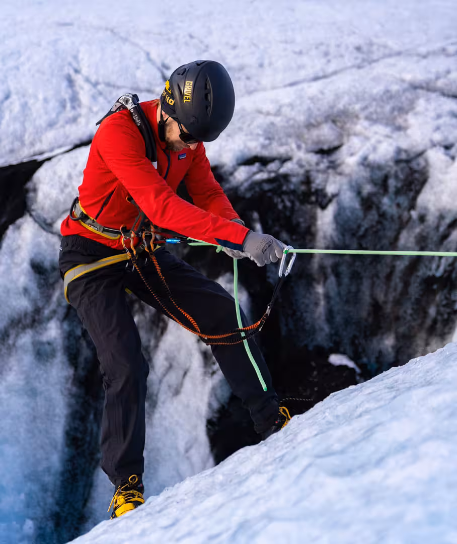 Guide rappelling into glacier crevasse on Solheimajokull Iceland wearing red jacket and safety harness
