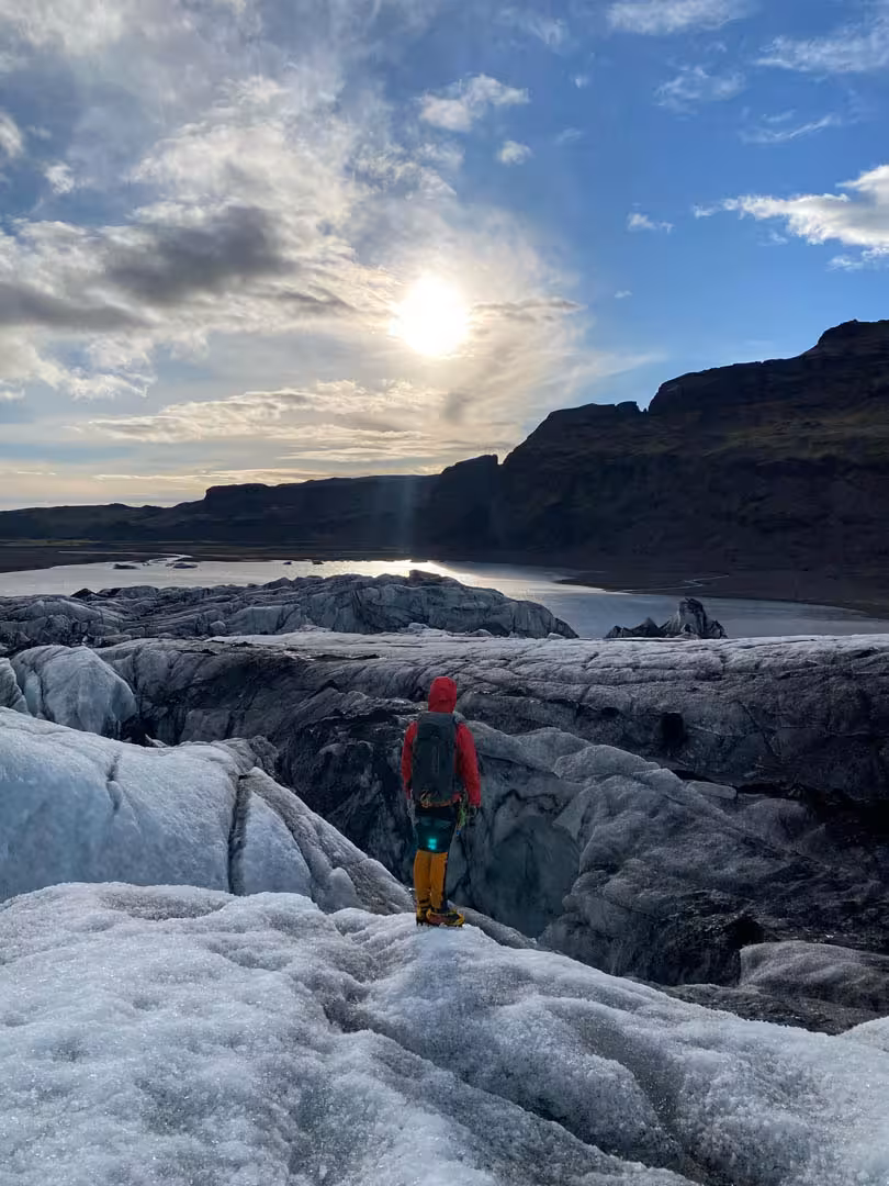 Hiker in red jacket standing on Solheimajokull glacier ice under midnight sun in Iceland