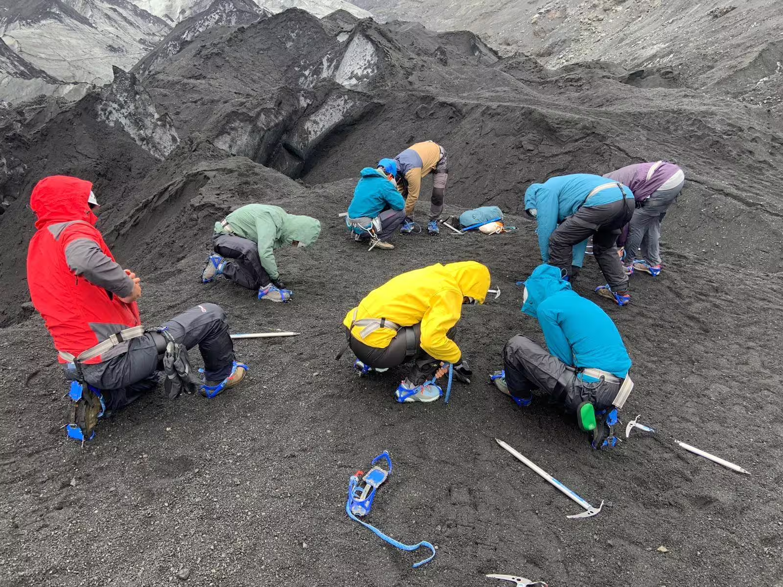 Group of hikers in colorful jackets kneeling on dark volcanic ash surface of Solheimajokull glacier Iceland
