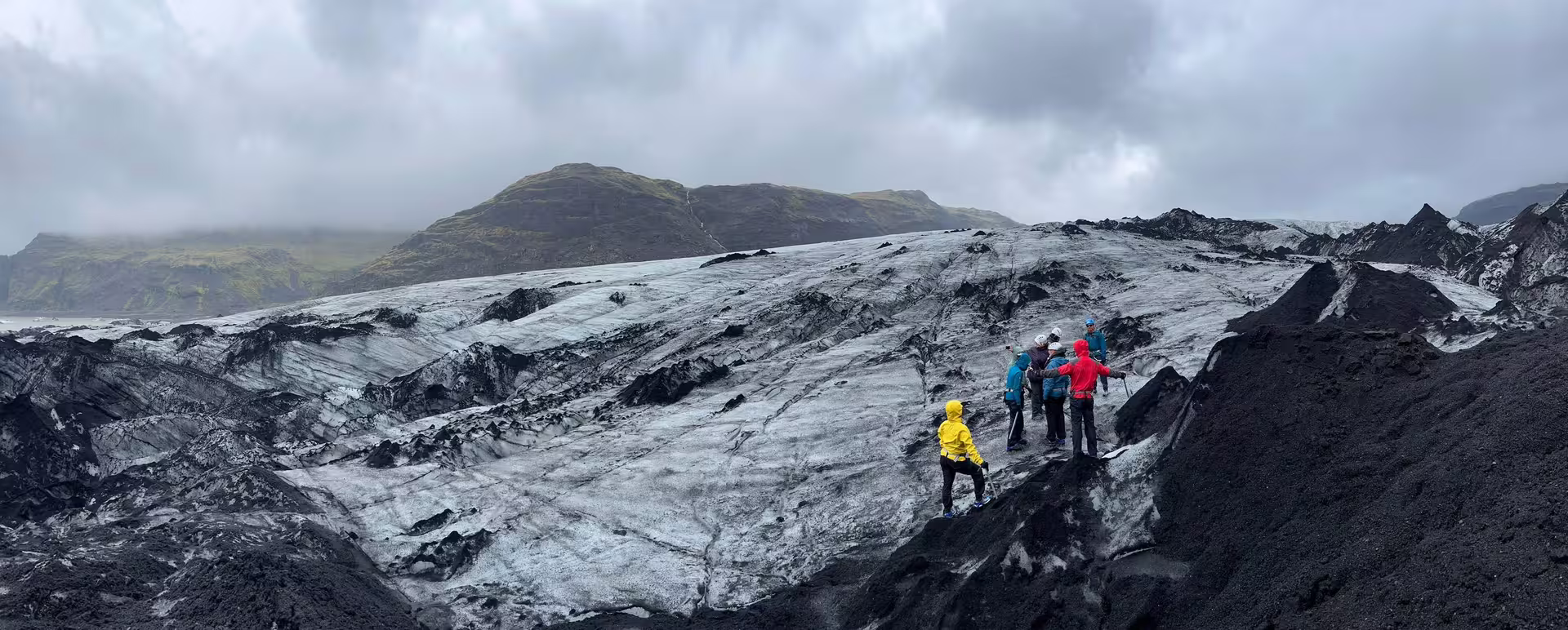 Small group of hikers in colorful jackets climbing the black ash-covered Solheimajokull glacier in Iceland