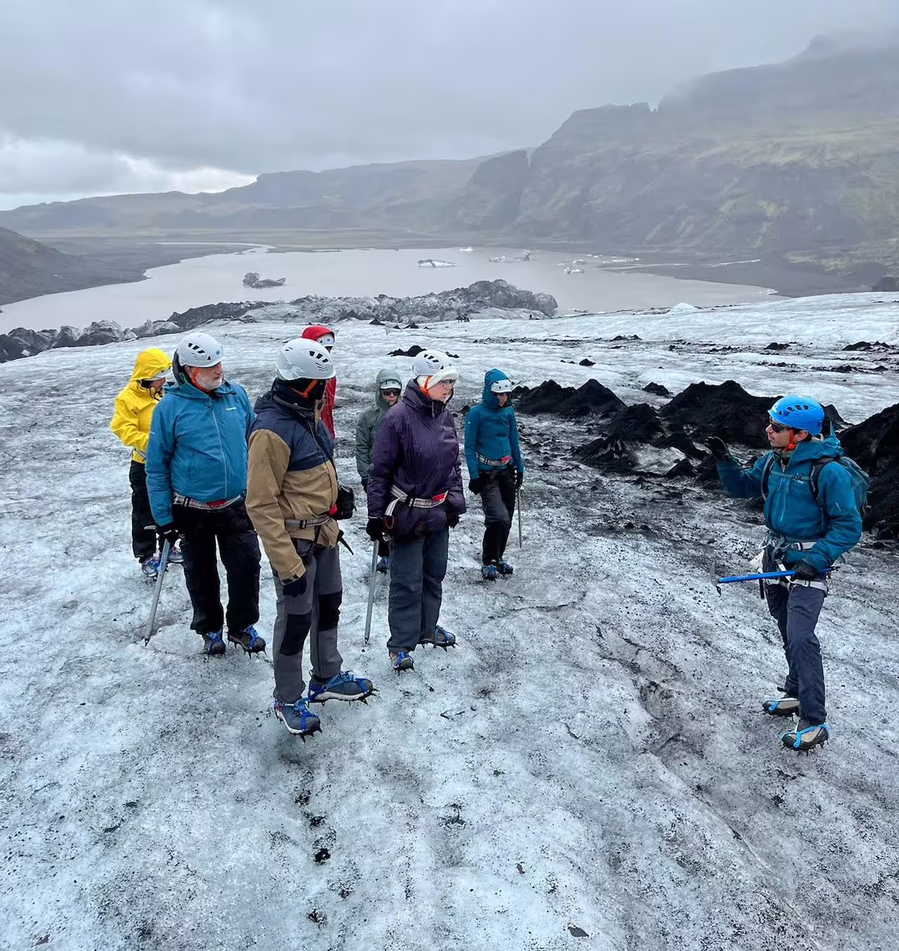 Small group of hikers with crampons and helmets receiving glacier hiking briefing on Solheimajokull Iceland
