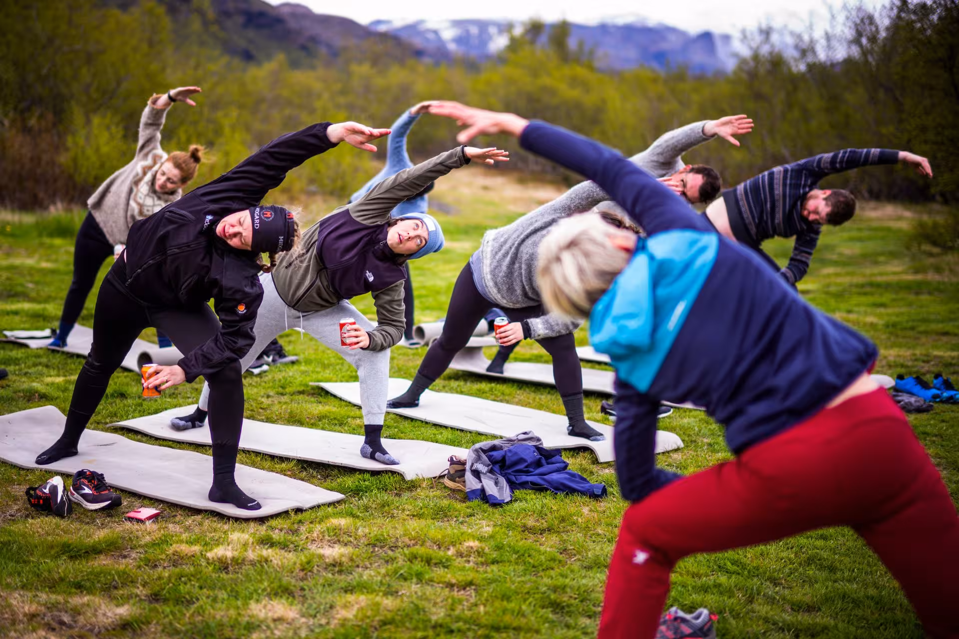 Group doing outdoor yoga stretches on mats in Icelandic landscape with mountains in background
