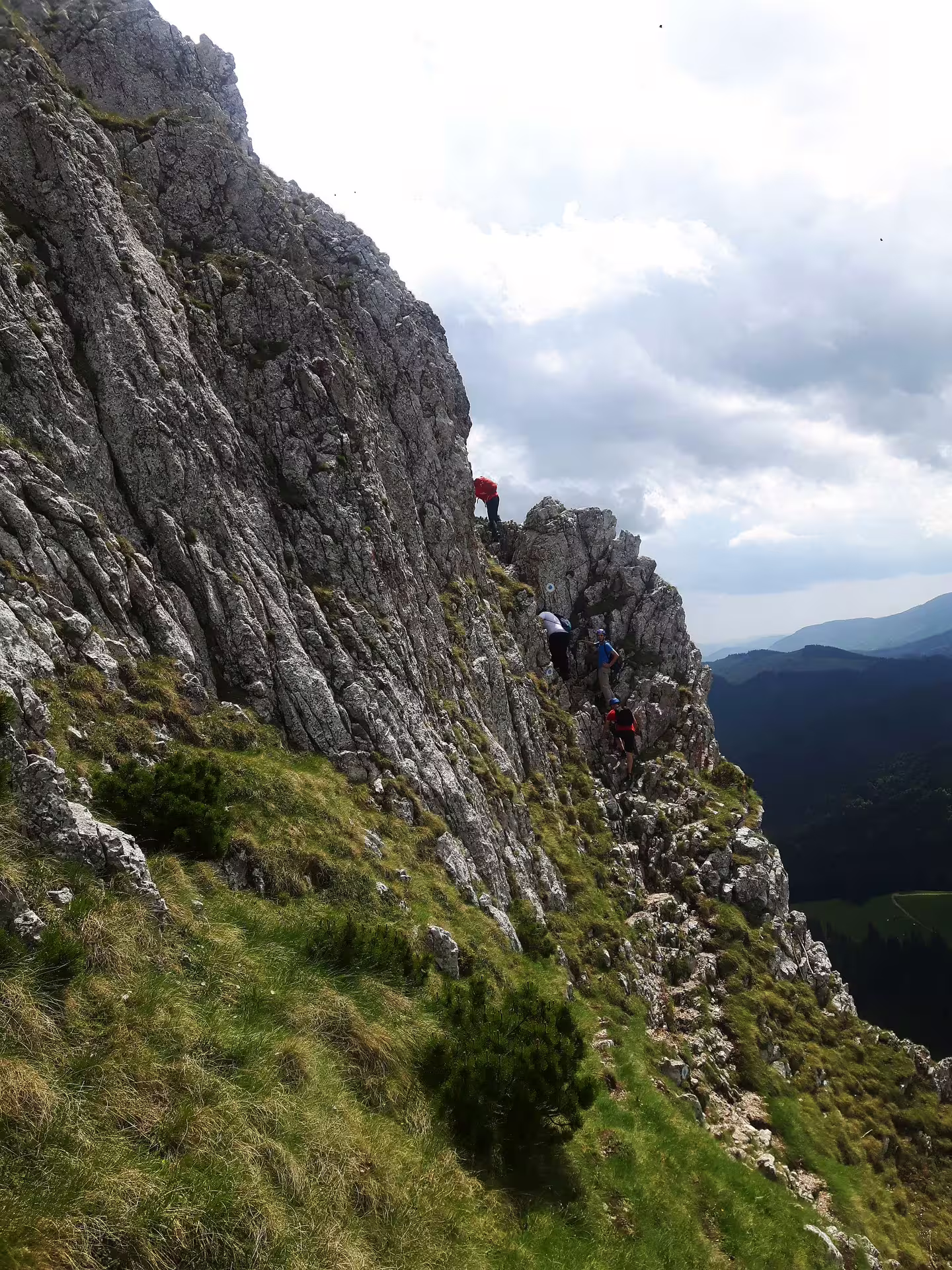 Hikers scrambling along the rocky Piatra Craiului Ridge with sweeping mountain valley views below