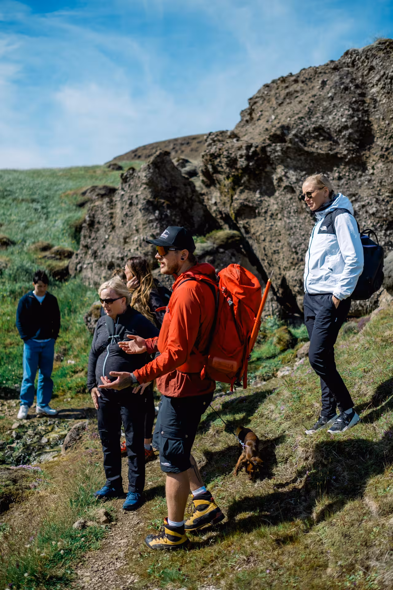 Tour guide in red jacket leading a group of hikers on a rocky volcanic trail in Iceland