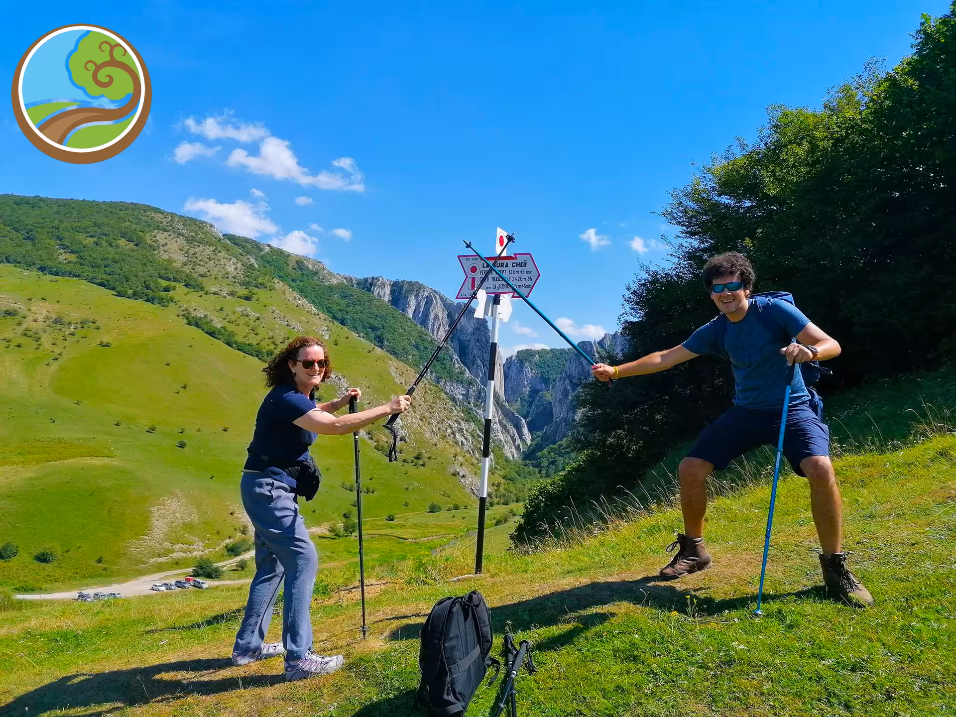 Two hikers with trekking poles posing at a trail signpost in Transylvania's green mountain landscape