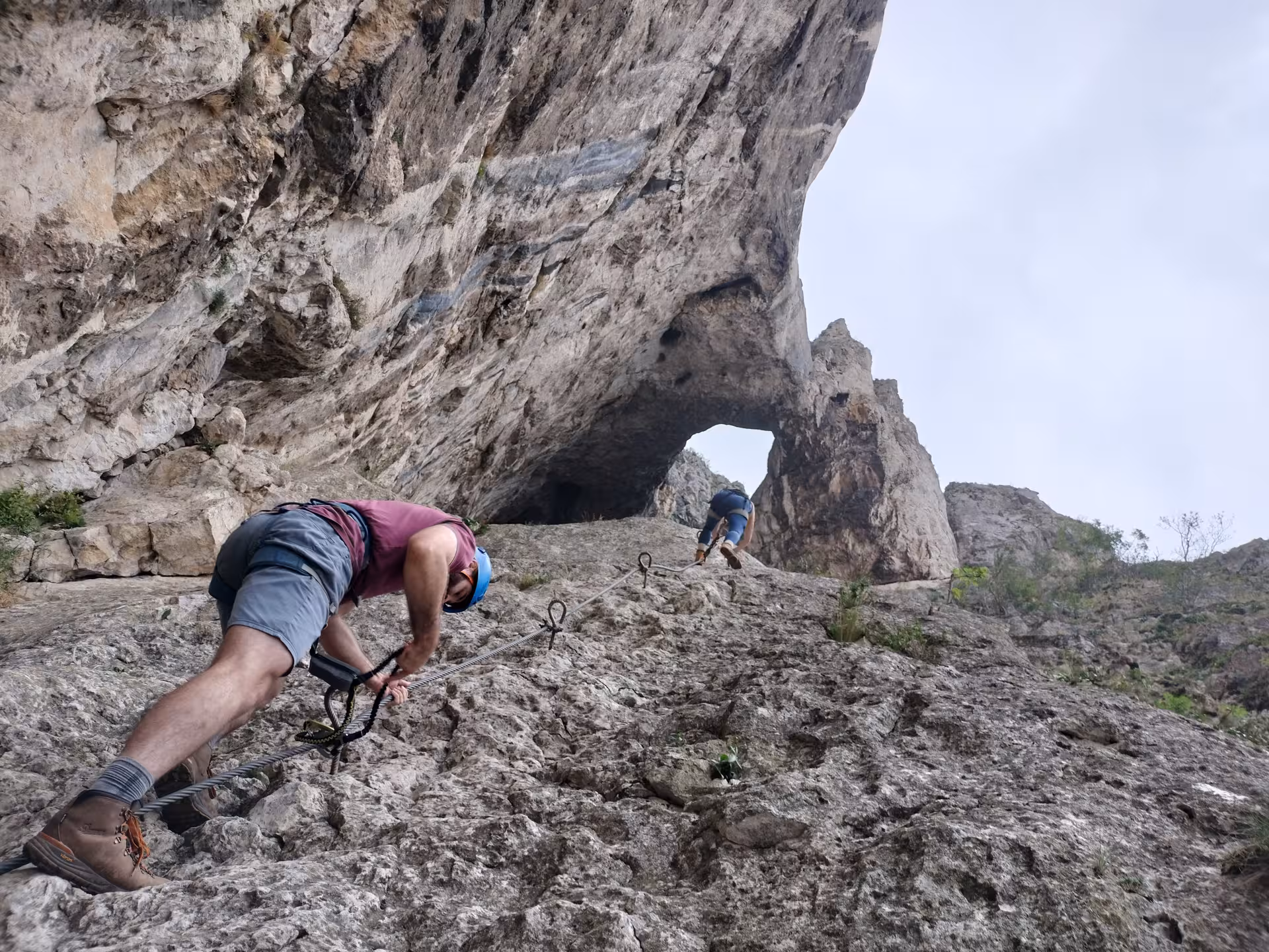 Two hikers climbing steep rocky slope with fixed cable on a guided tour in Turda Canyon
