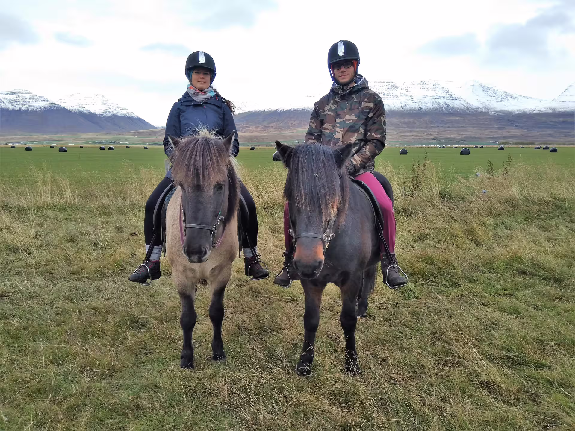 Two riders on Icelandic horses in Skagafjordur valley with snow-capped mountains in background