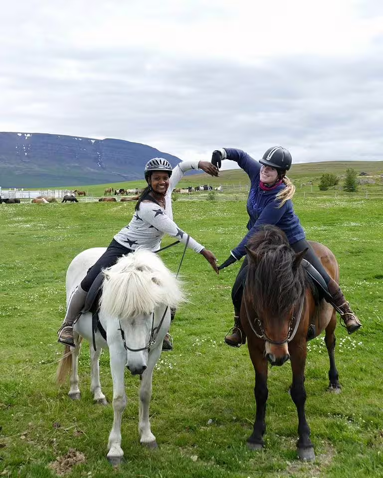 Two riders on Icelandic horses in green Skagafjordur valley, forming a heart with their arms