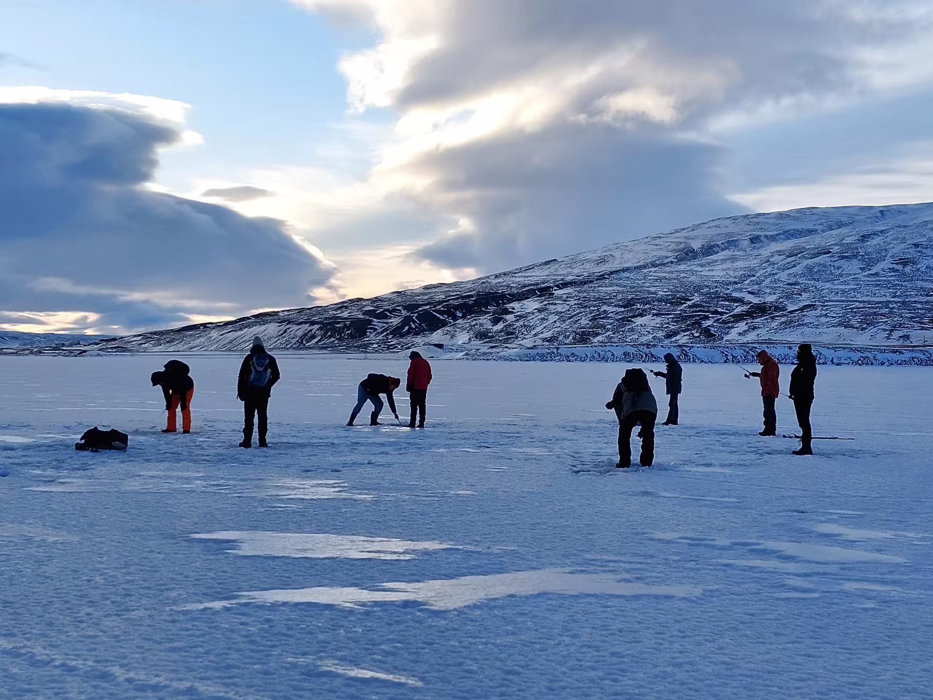 Group of people ice fishing on a frozen lake in Akureyri with snowy mountains in the background
