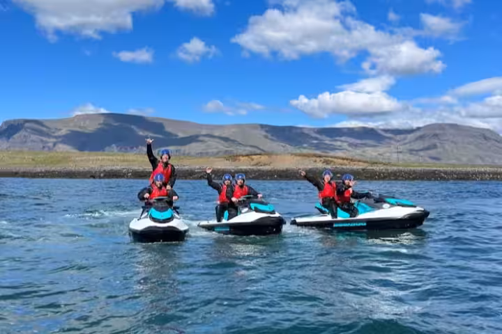 Three jet skis with riders in red life jackets and blue helmets on Reykjavik Bay with mountains behind