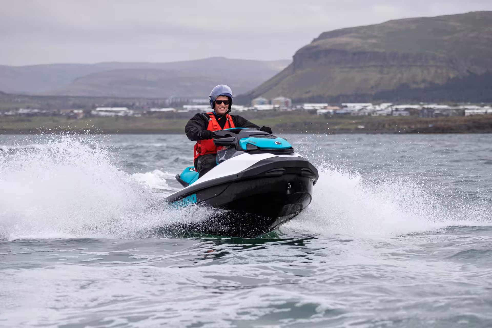 Smiling rider on a Sea-Doo jet ski speeding across Reykjavik Bay with mountain backdrop
