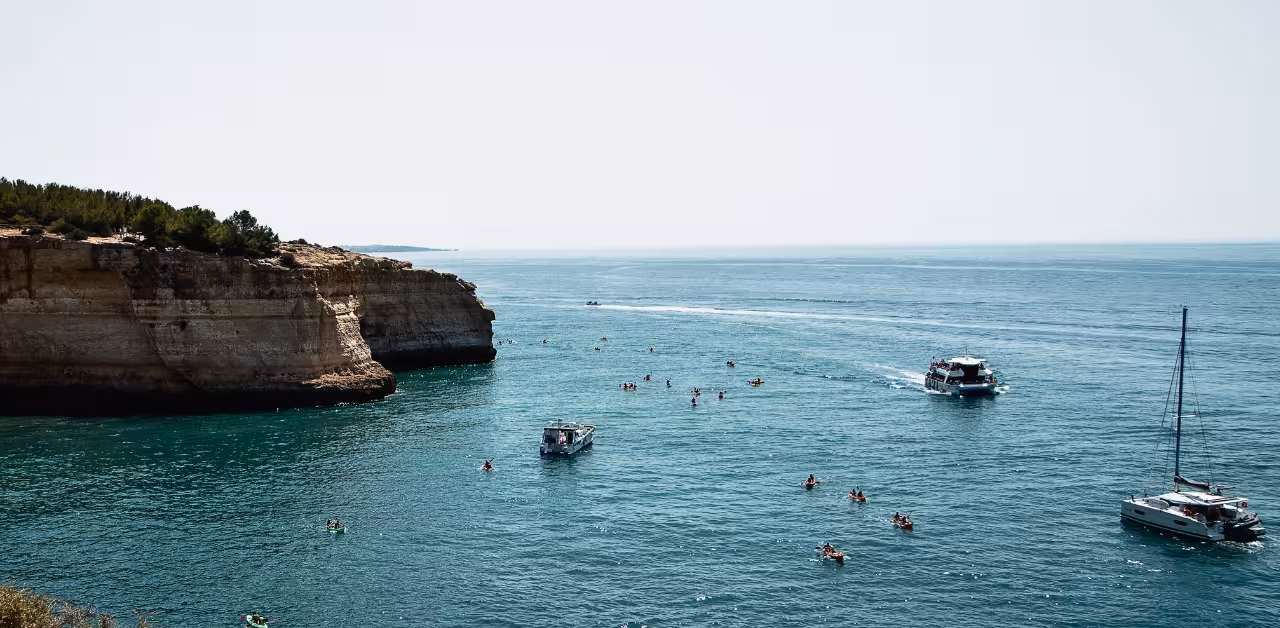 Guided kayak adventure near Benagil Caves with boats, swimmers and dramatic Algarve sea cliffs on a sunny Portugal day