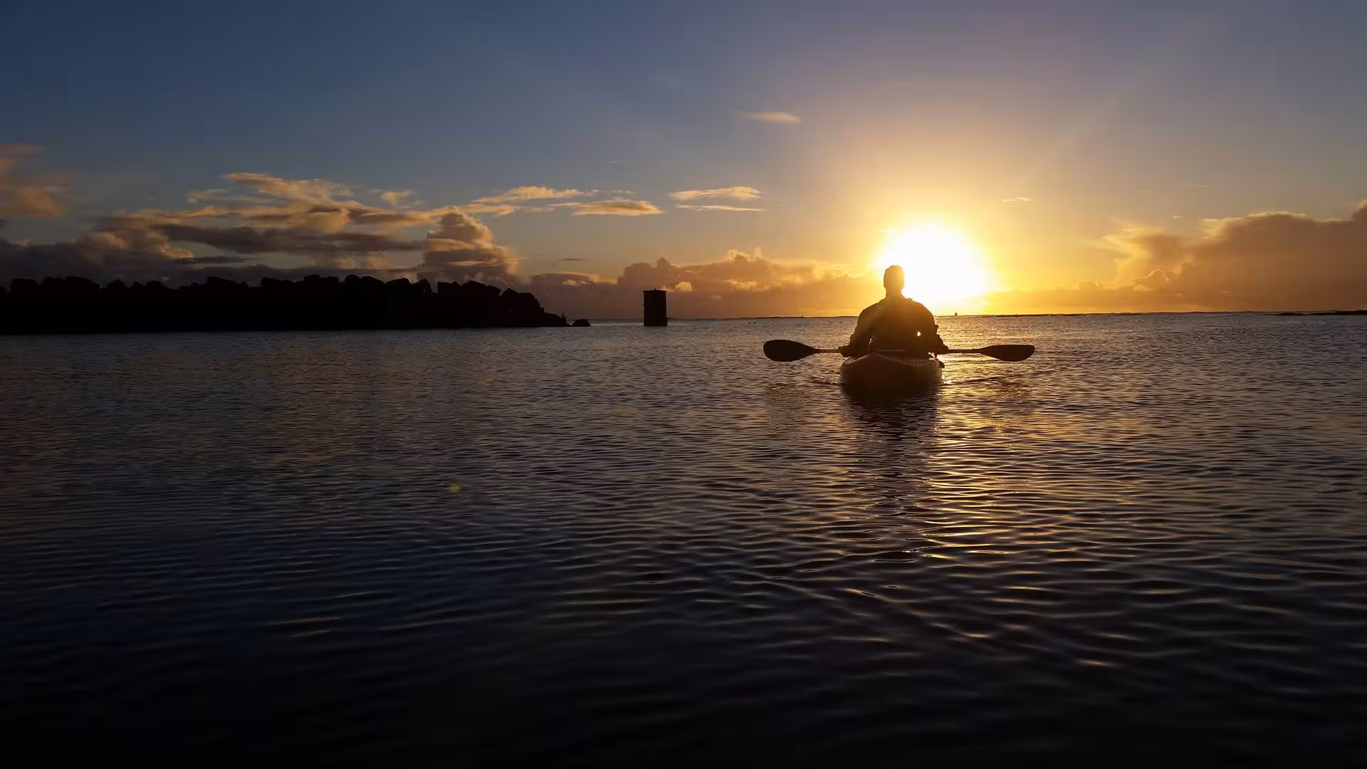 Kayaker silhouetted against golden sunset on calm Icelandic waters during guided kayak tour