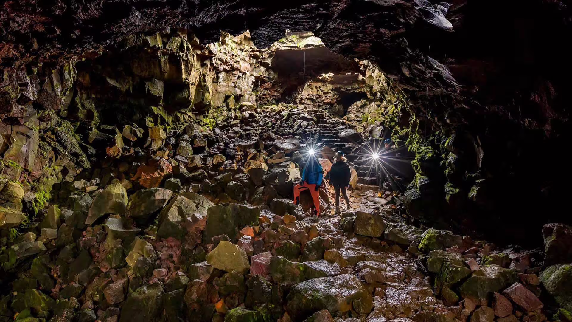 Explorers with headlamps walking through a rocky lava tunnel cave in Iceland