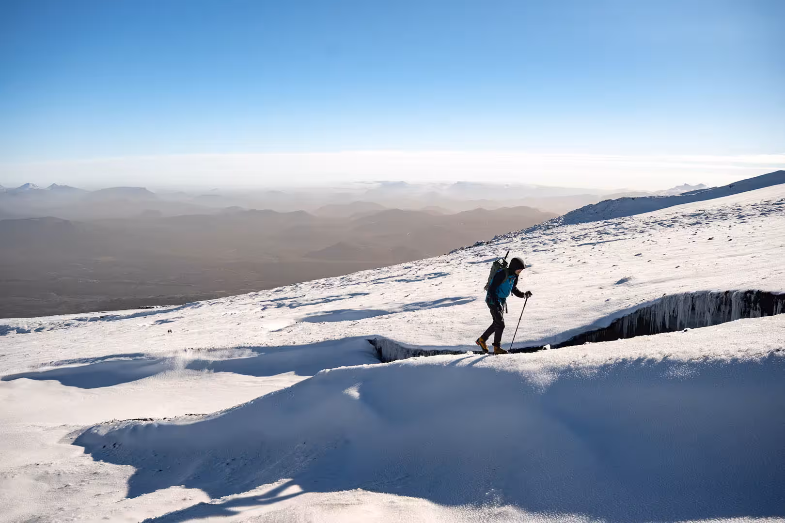 Mountaineer with trekking poles climbing snowy Snaefellsjokull glacier slope with vast Iceland landscape below
