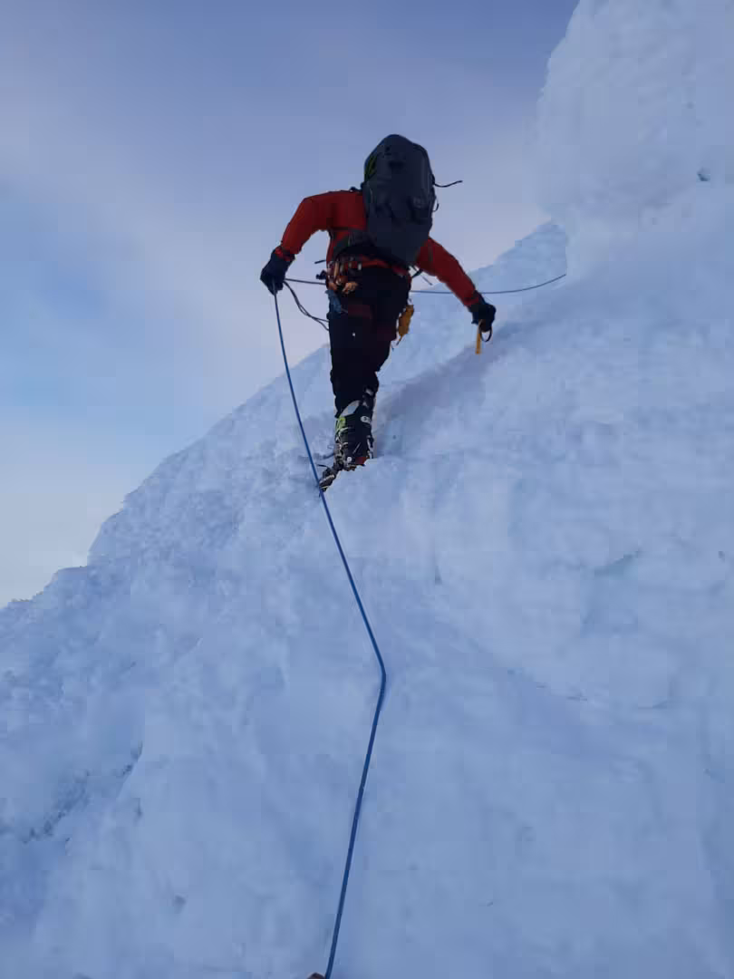 Climber ascending steep snowy ridge at Snaefellsjokull glacier with blue rope and crampons