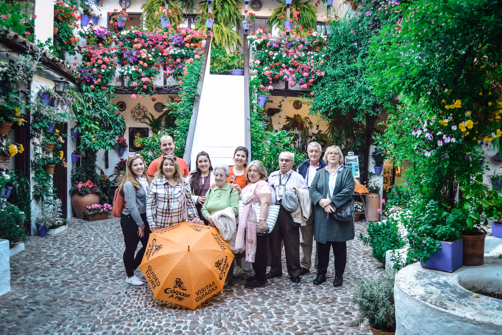 Group of tourists enjoying a guided tour in Córdoba's flower-filled patio, surrounded by vibrant hanging plants.