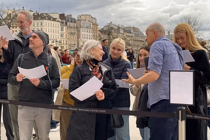 Tourists holding papers queue at Notre-Dame entrance barrier in Paris with Haussmann buildings in background