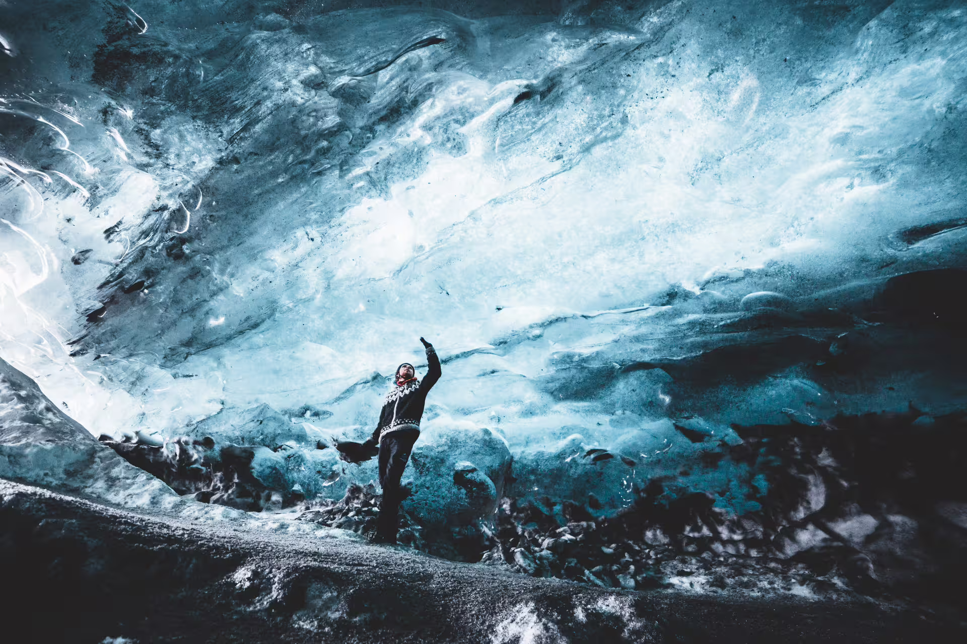 Traveler reaching up inside a stunning blue glacial ice cave on Iceland's South Coast tour