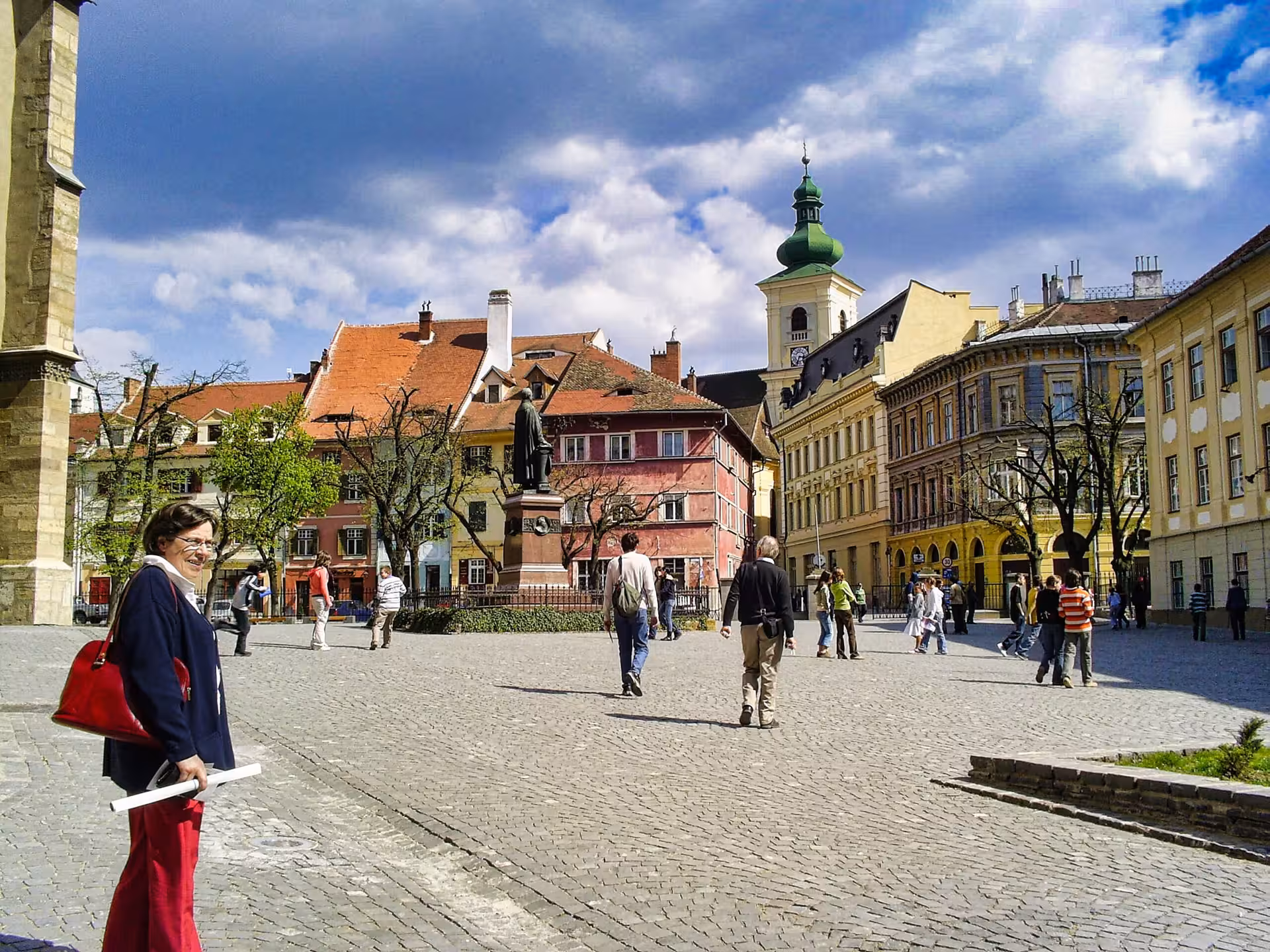 Tourists walking through Sibiu's cobblestone Grand Square with colorful historic buildings and church tower