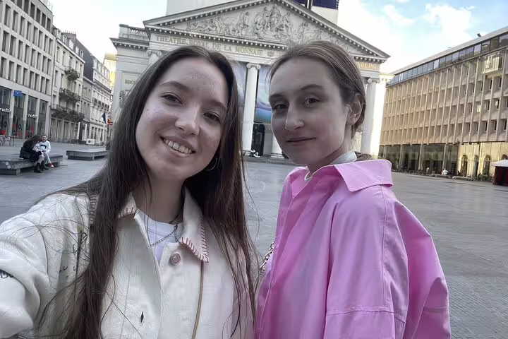 Two young women smiling in Brussels city square with Théâtre Royal de la Monnaie in background