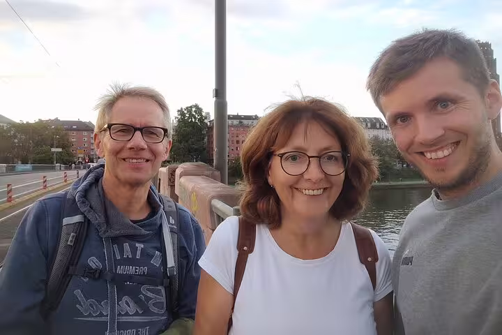 Three smiling tourists on a bridge during a guided walking tour of Frankfurt Old Town