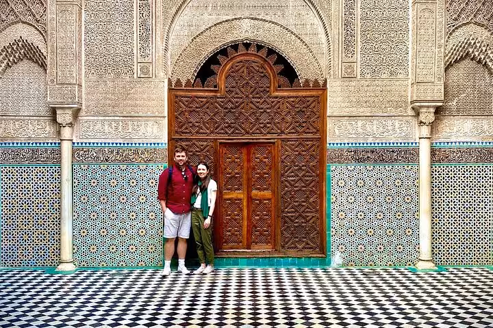 Visitors admire intricate tilework and carvings at a historic madrasa in Fez's Old Medina.
