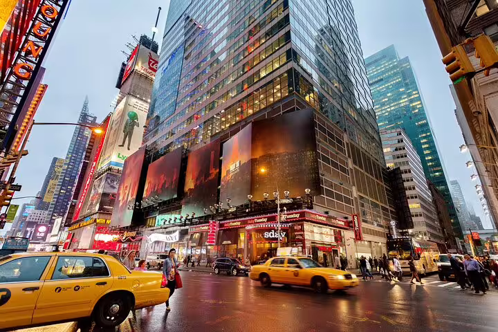Yellow taxis passing through Times Square in Midtown Manhattan at dusk with illuminated billboards