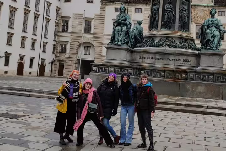 Five tourists posing in front of Emperor Franz monument at Vienna's Hofburg Palace on a guided walking tour