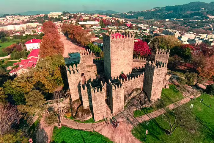 Aerial view of the historic Guimarães Castle surrounded by lush greenery on a sunny day, perfect for cultural exploration.
