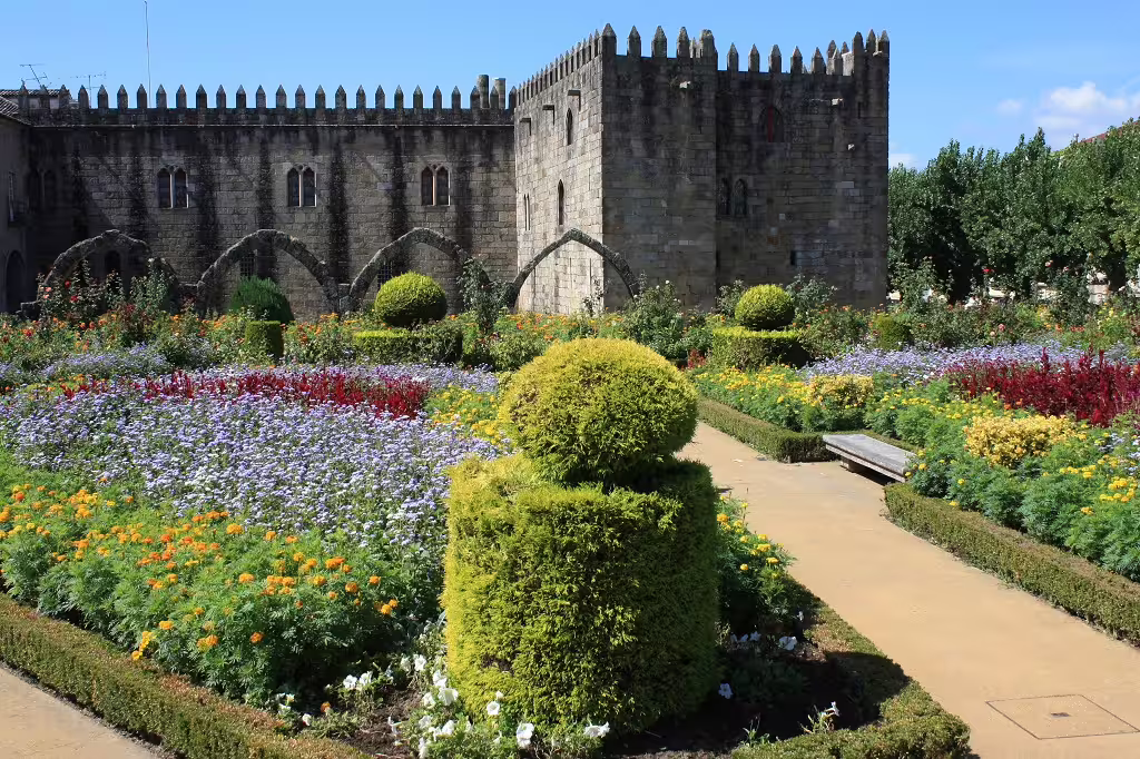 Historic Guimarães Castle with vibrant flower gardens in Portugal, showcasing medieval architecture and lush landscapes.