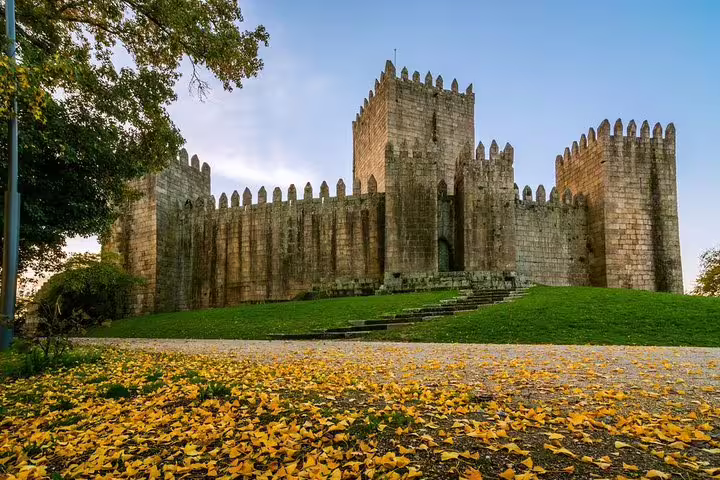 Explore the medieval charm of Guimarães Castle on a private half-day tour from Porto, surrounded by autumn foliage.