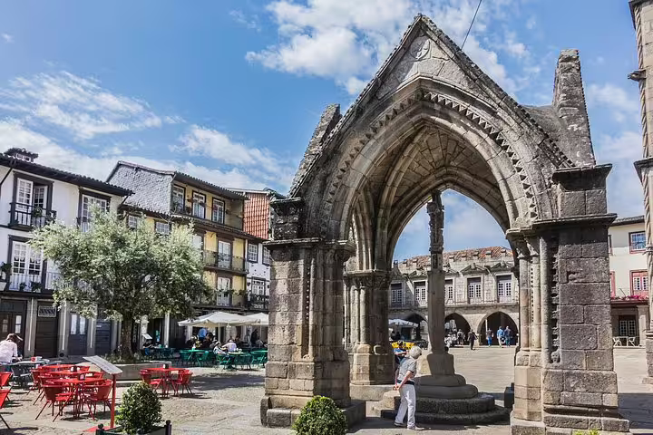 Historic square in Guimarães with medieval architecture, vibrant cafes, and iconic stone monument under a blue sky.