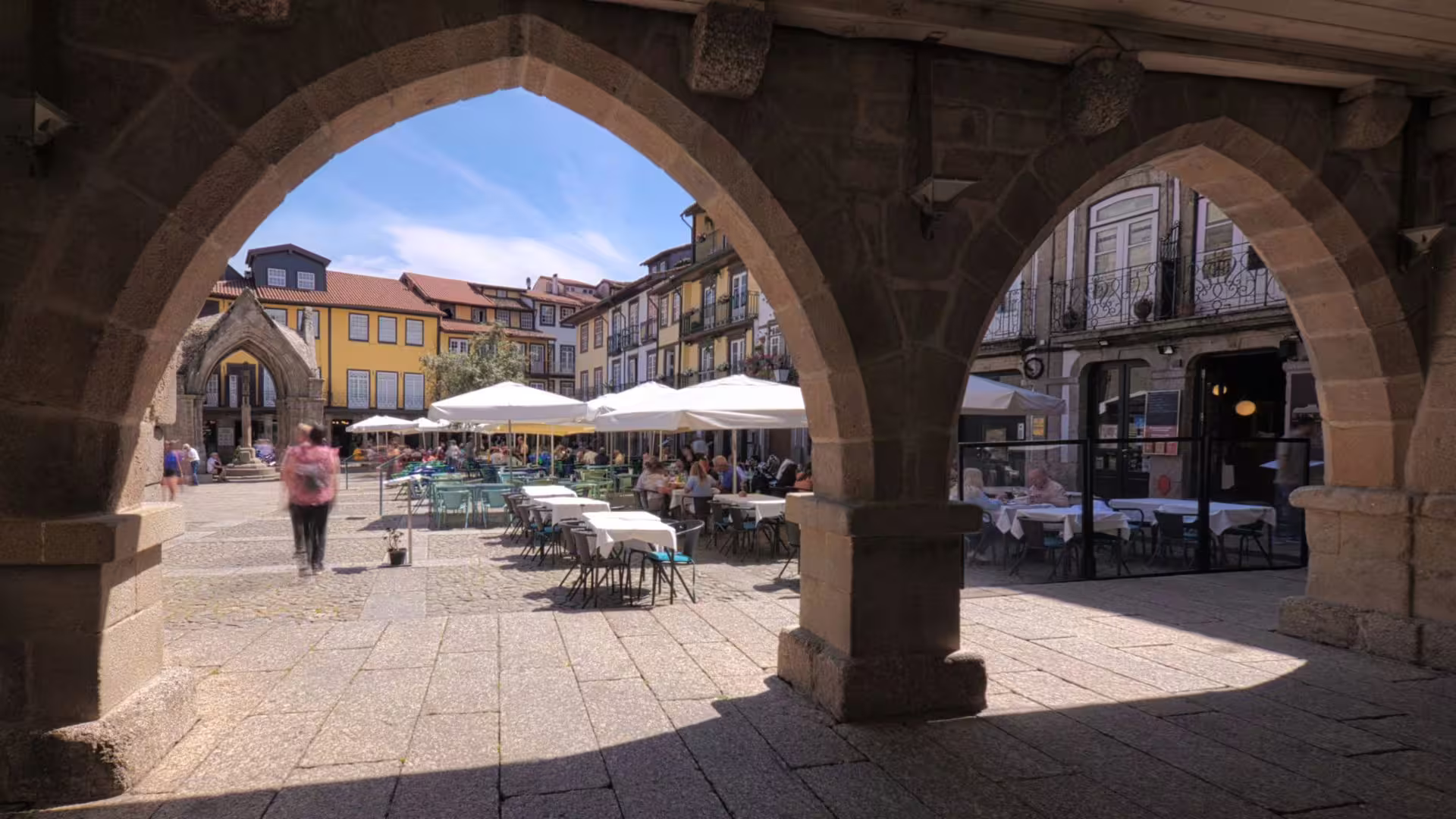 Vibrant outdoor café scene in a historic square in Guimarães under stone arches.