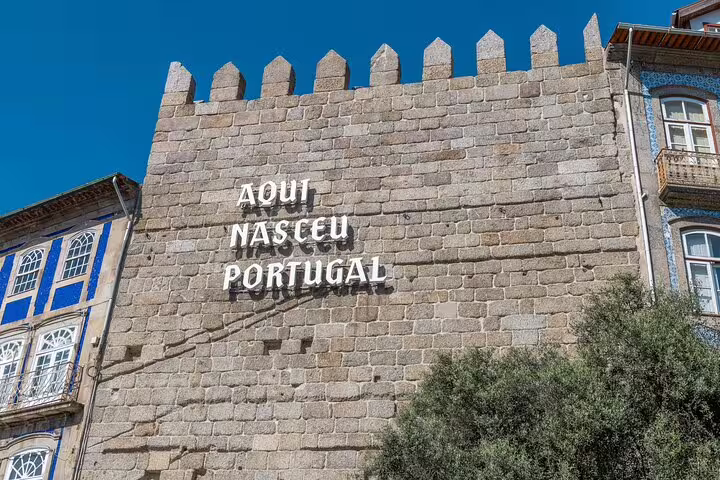 Historic stone wall with 'Aqui Nasceu Portugal' inscription in Guimarães on a sunny day.