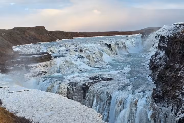 Gullfoss waterfall partially frozen in winter with cascading water and snow-covered rocks in Iceland