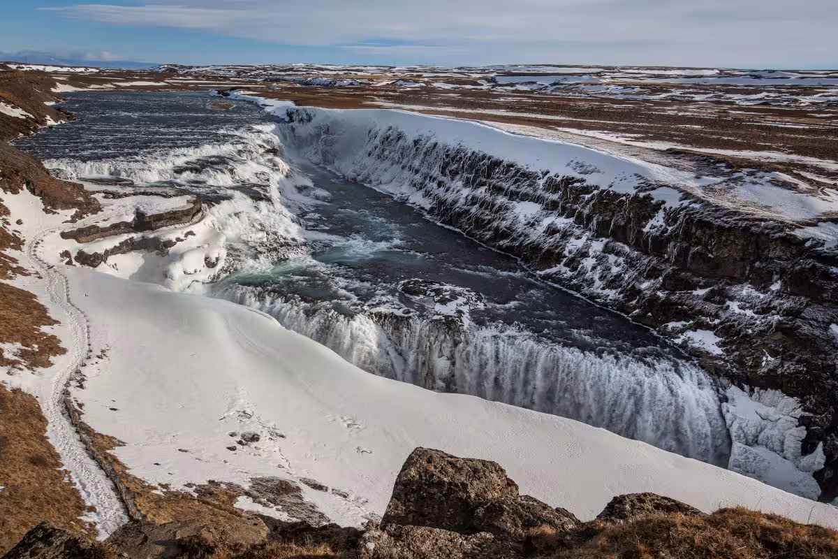Majestic Gullfoss waterfall partially frozen in Iceland's winter landscape on a glacier lagoon tour.
