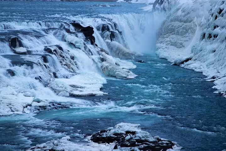 Gullfoss waterfall partially frozen in winter with turquoise glacial river flowing through icy canyon