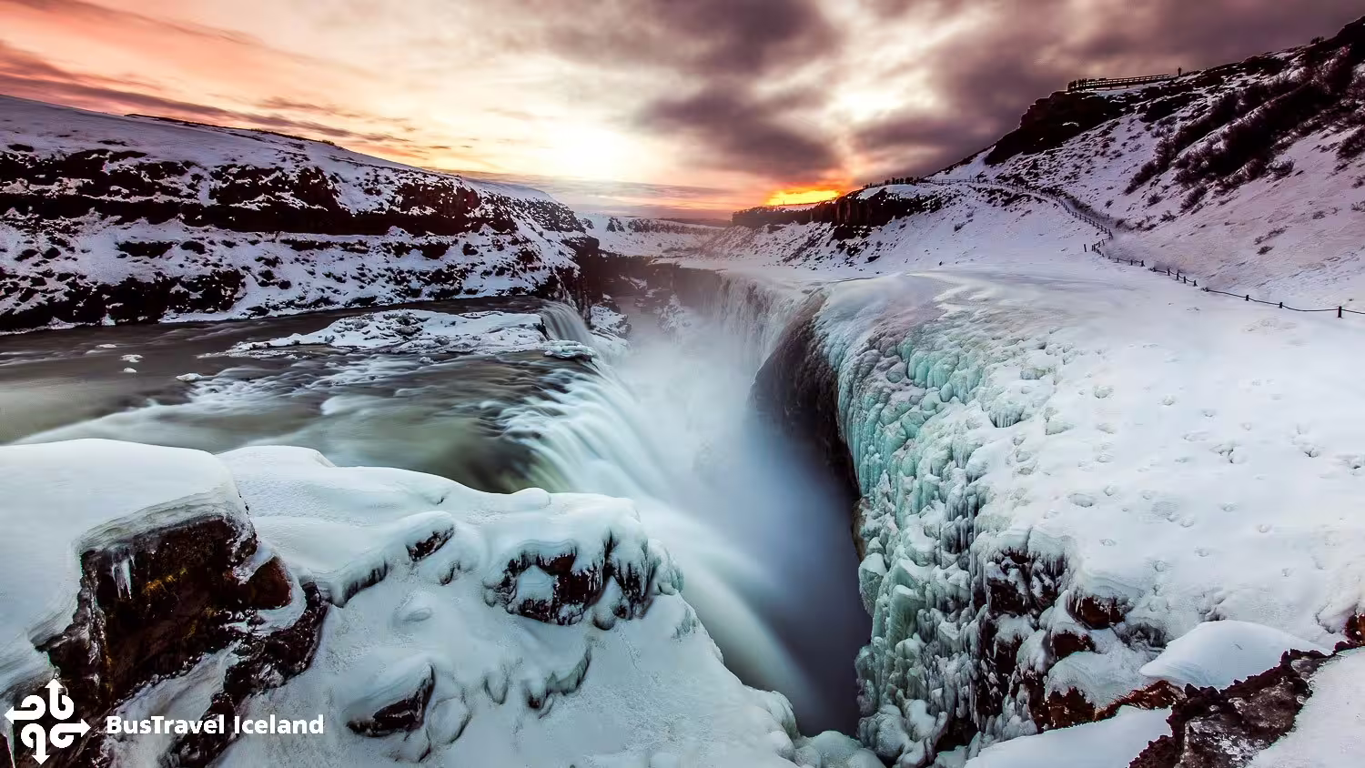 Gullfoss waterfall frozen in winter with snow-covered canyon and dramatic sunset sky, Golden Circle Iceland